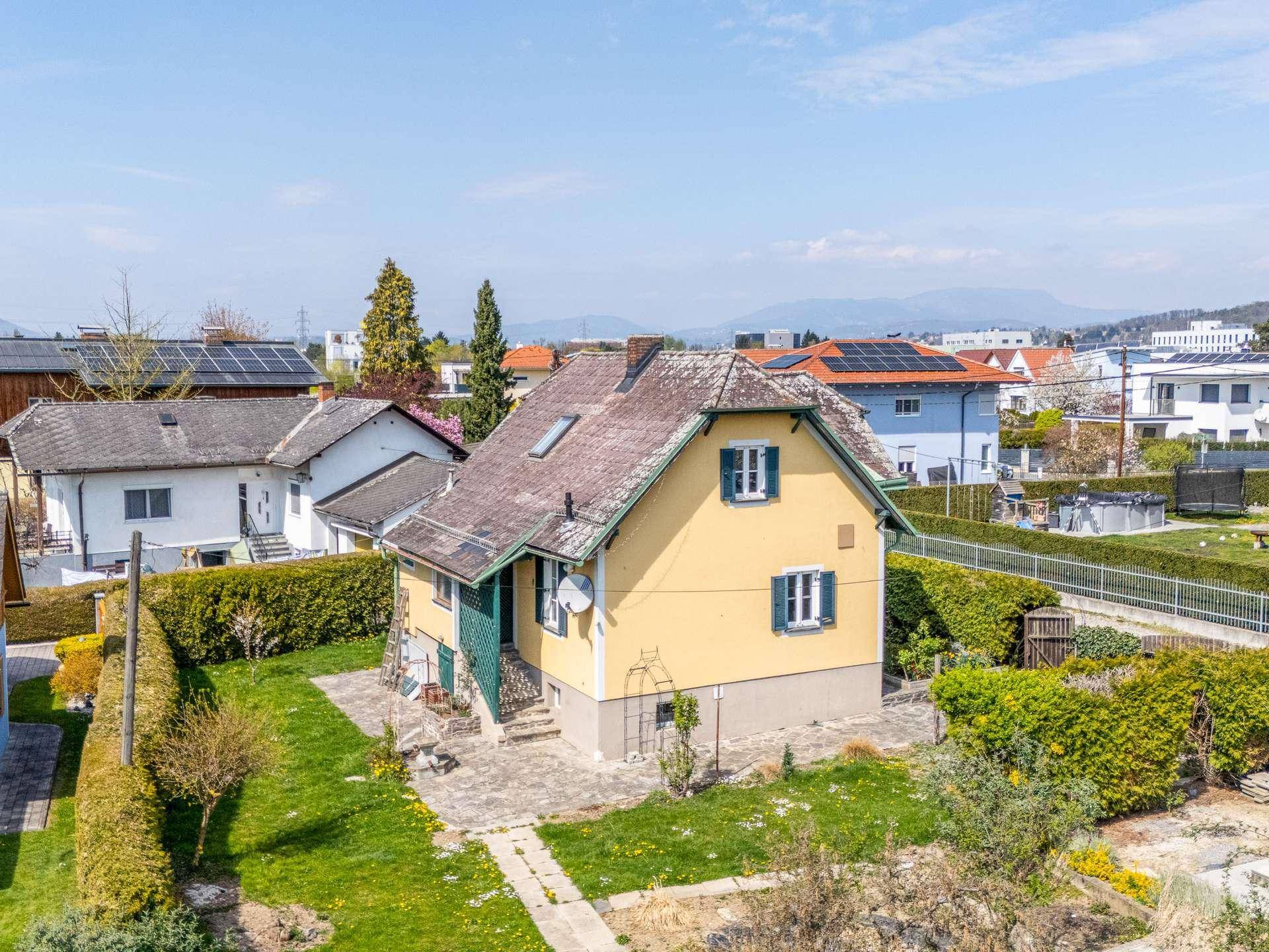 Luftaufnahme eines gelben Einfamilienhauses mit Satteldach und grünen Fensterläden in ländlicher Umgebung.