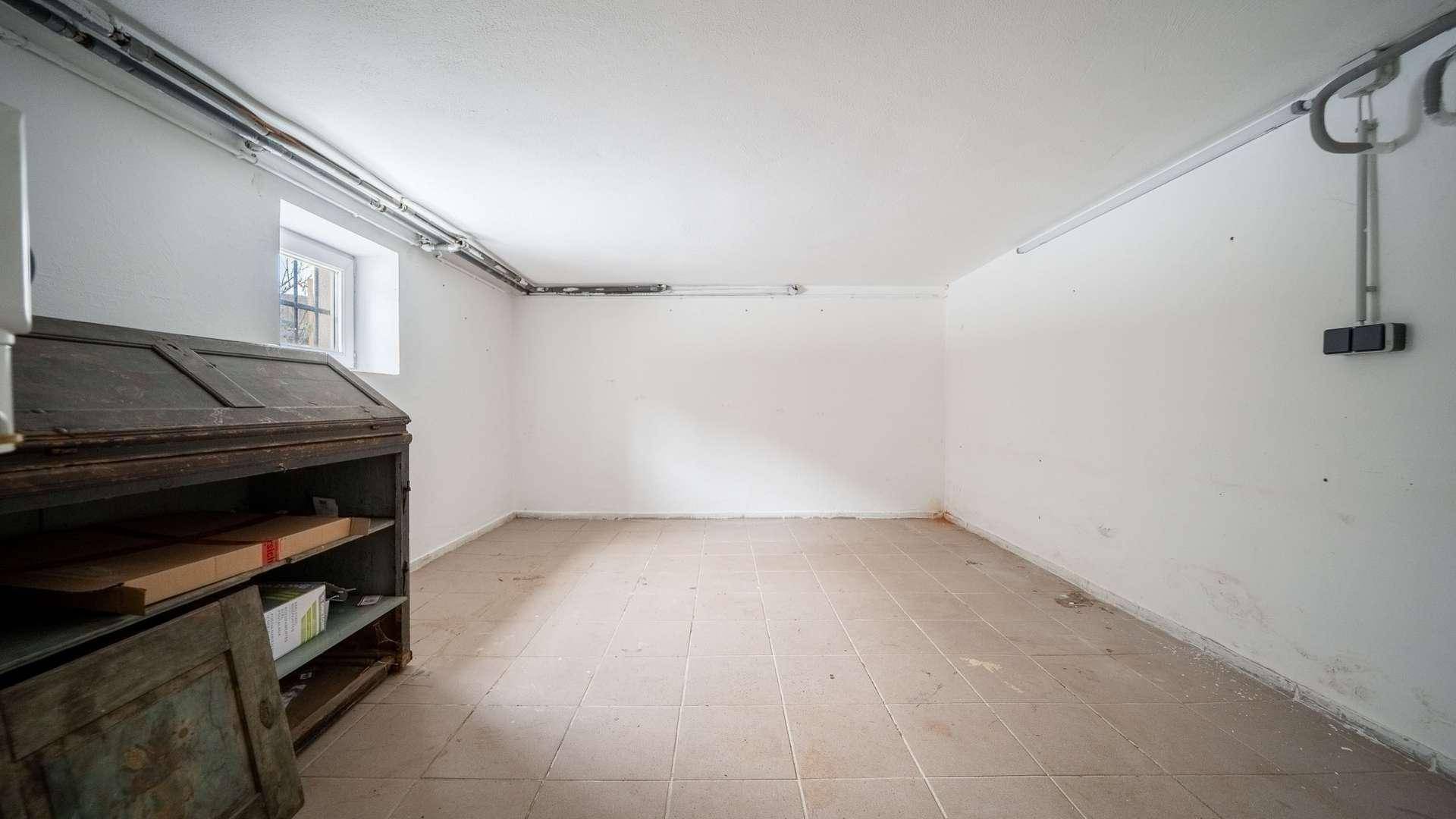 Kellerraum mit Fliesenboden, kleinem Fenster und einem alten Schrank.