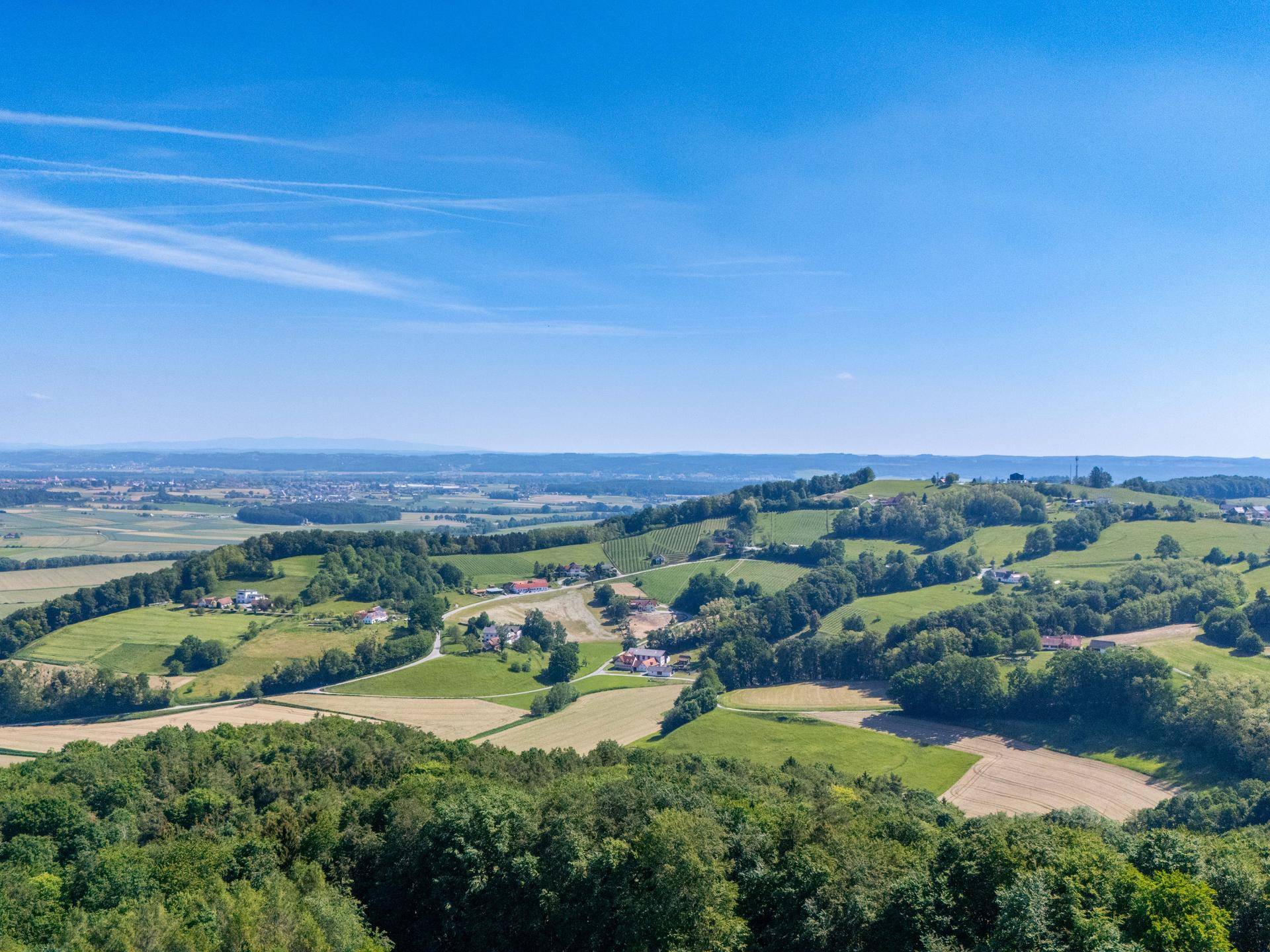 Panoramablick über weite Felder, Wälder und sanfte Hügel unter blauem Himmel.