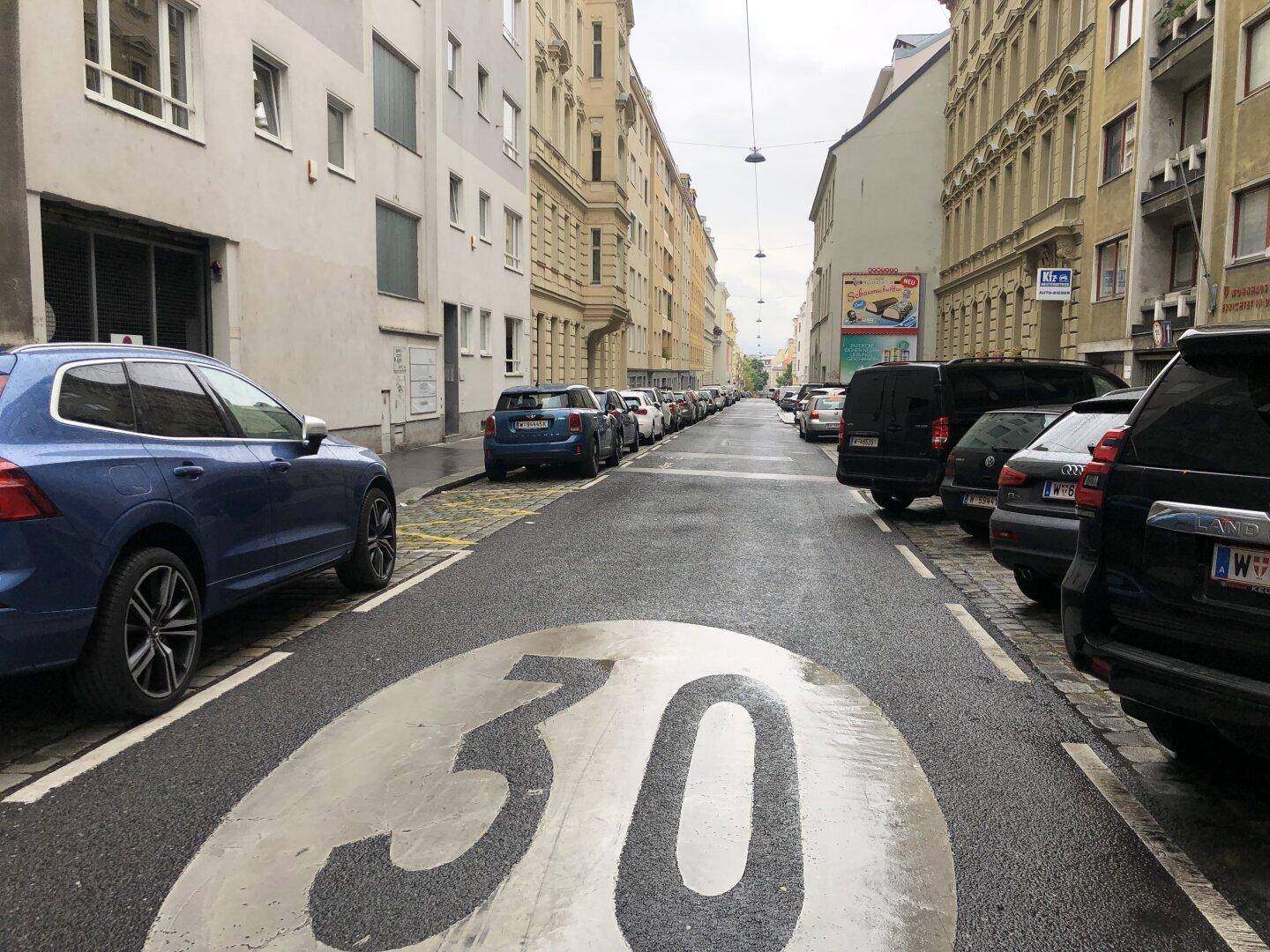 Stadtstraße mit geparkten Autos, Gebäuden und einer Geschwindigkeitsbegrenzung von 30 auf dem Asphalt.