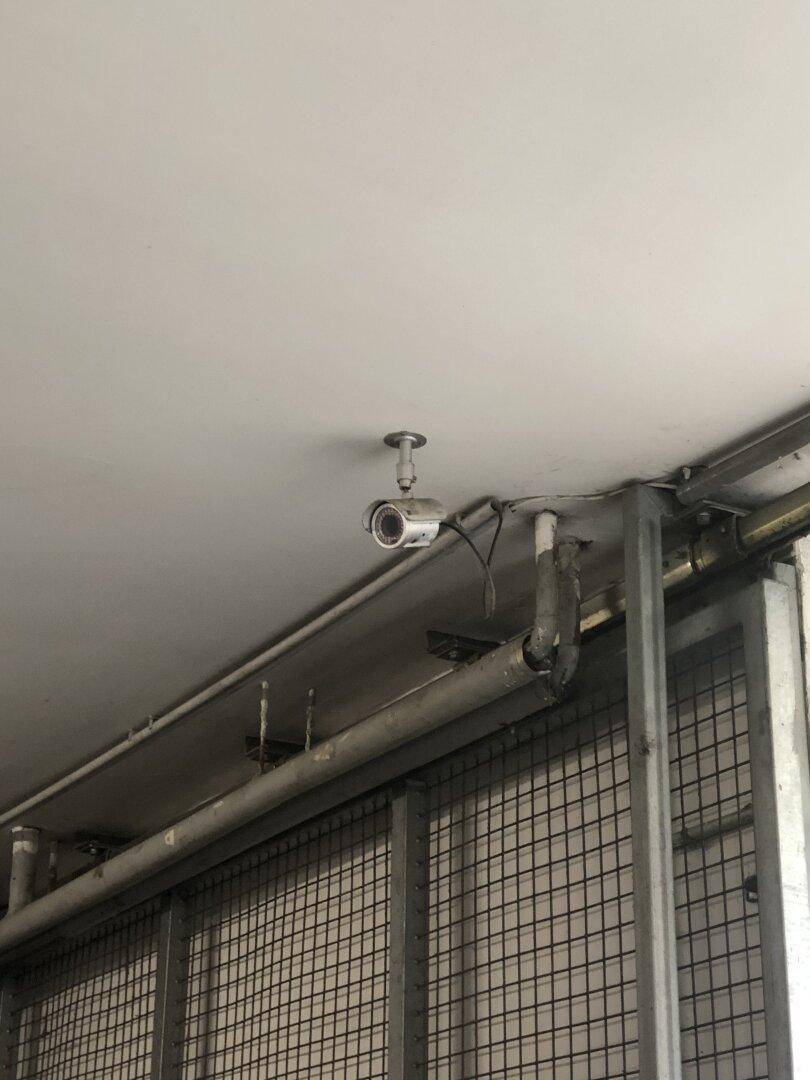 Überwachungskamera an der Decke einer Tiefgarage, montiert über einem Metallgitter für Sicherheit.