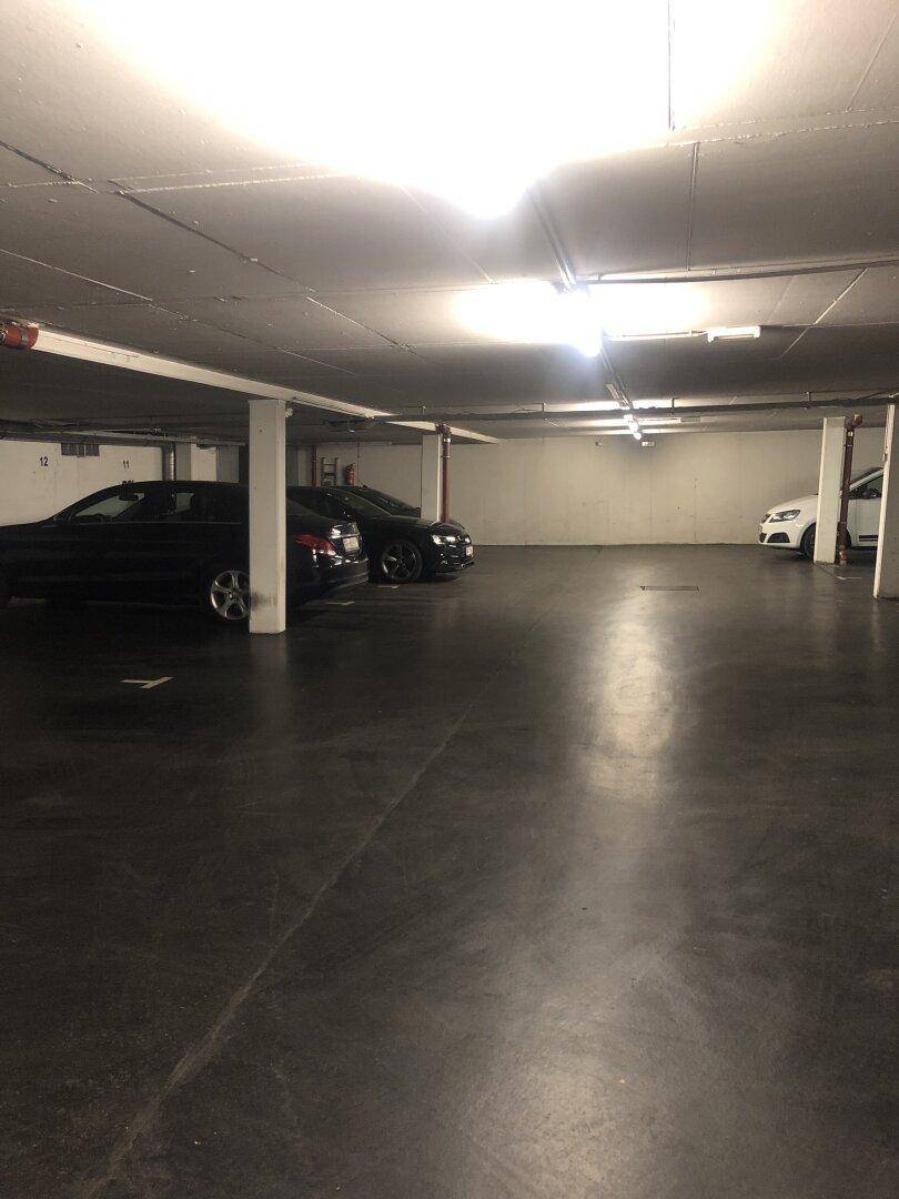 Geräumige Tiefgarage mit mehreren geparkten Autos, Betonpfeilern und heller Deckenbeleuchtung.