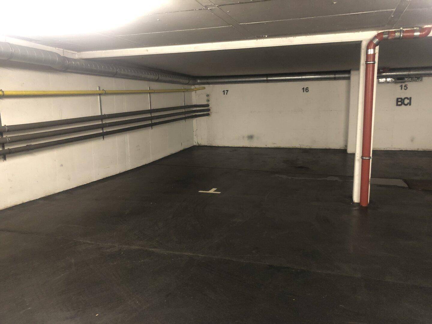 Leerer Stellplatz in einer Tiefgarage mit sichtbaren Rohren an der Wand und einer Betondecke.