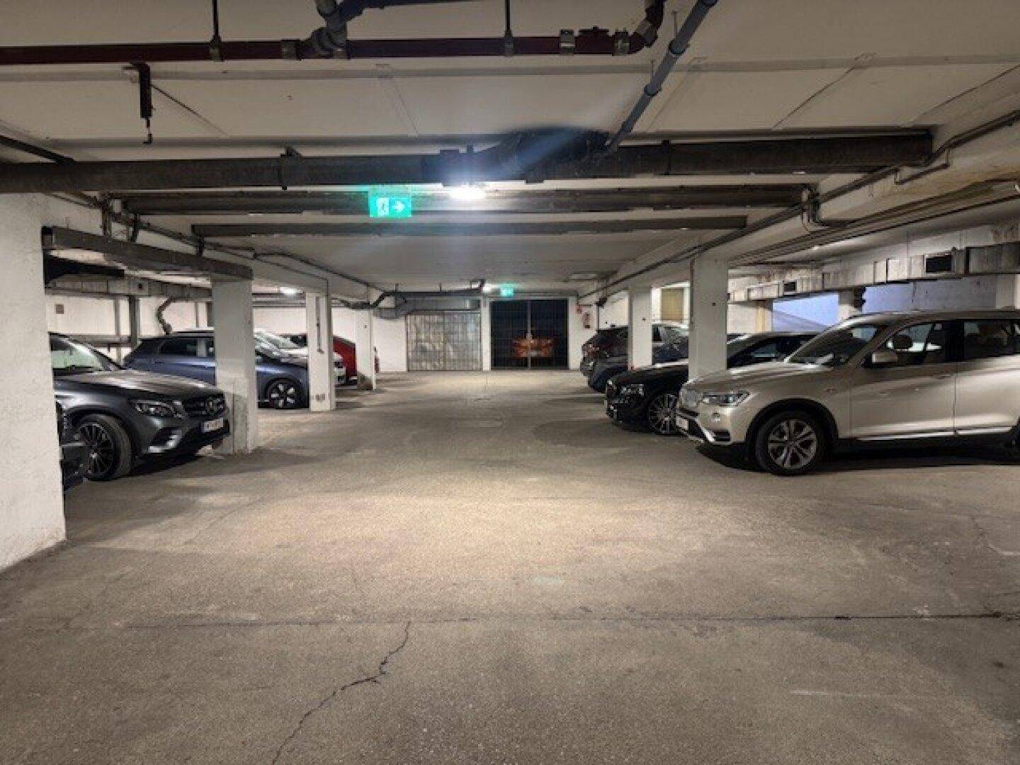 Helle Tiefgarage mit vielen geparkten Fahrzeugen und einem sichtbaren Ausgangsbereich.