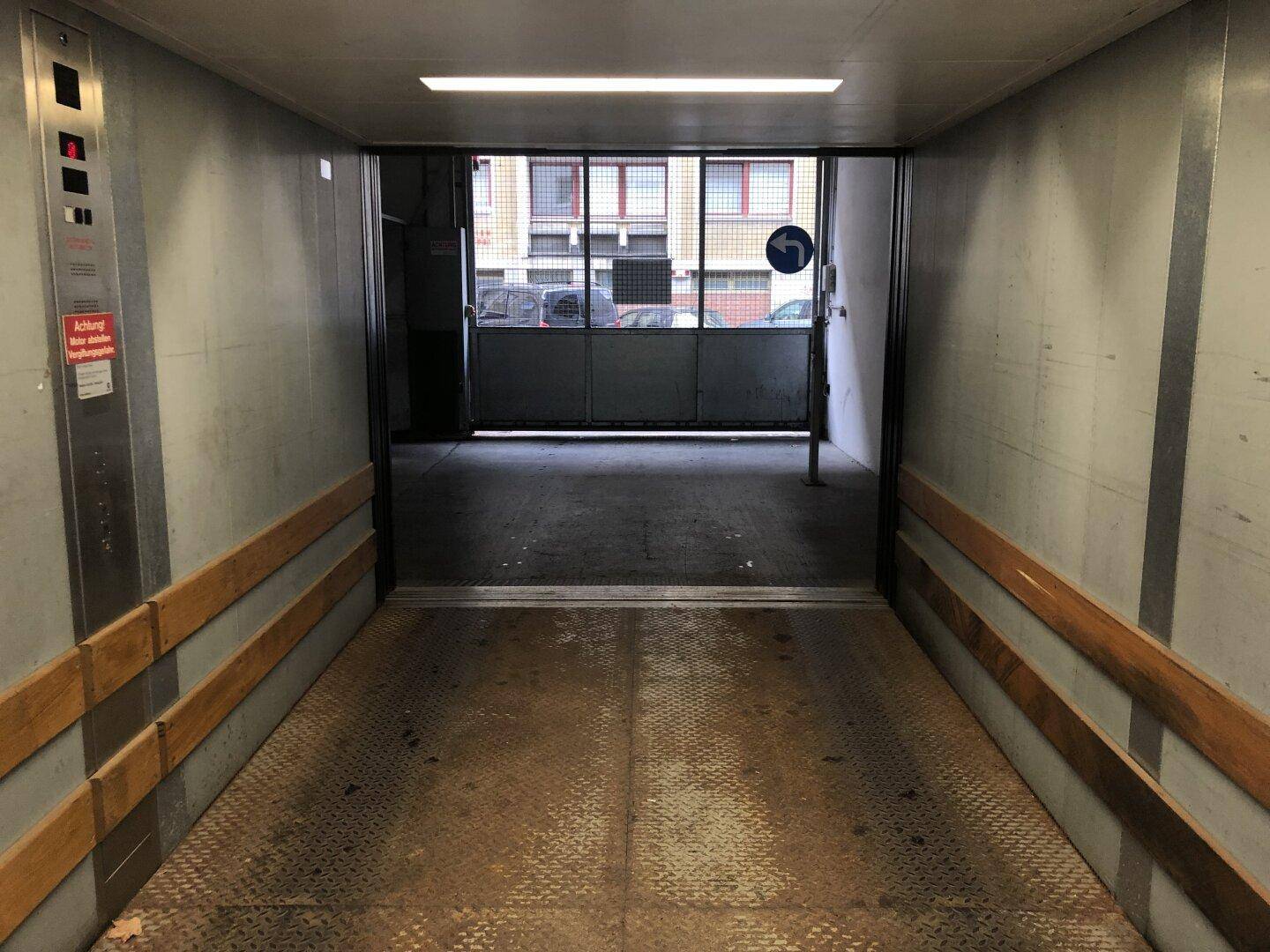Innenansicht eines Autoaufzugs oder einer Rampe, die zu einer Tiefgarage führt, mit Blick auf das Ausgangstor.