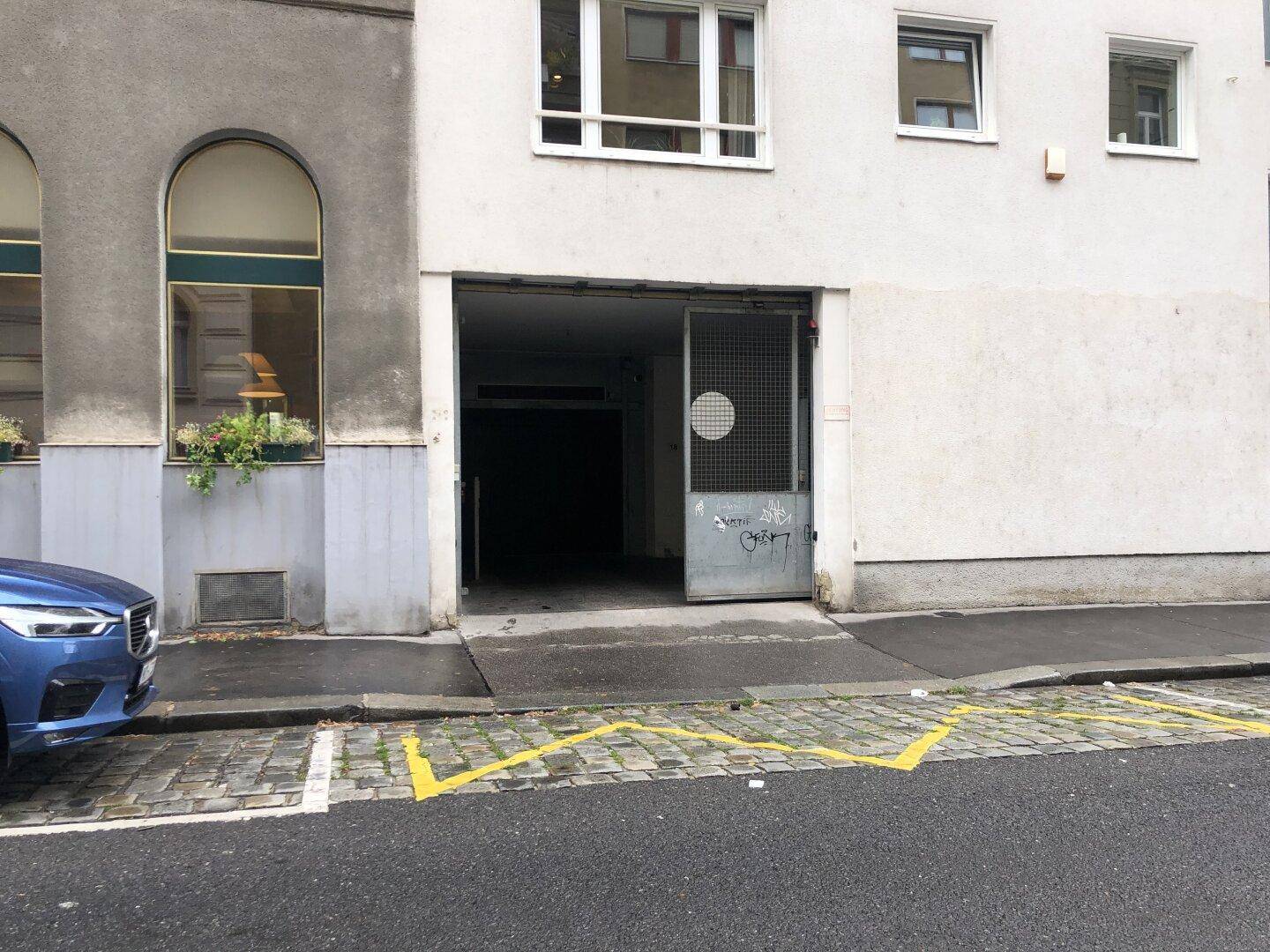 Eingang zu einer Tiefgarage von der Straße aus gesehen, mit einem geparkten Auto und gelben Markierungen.