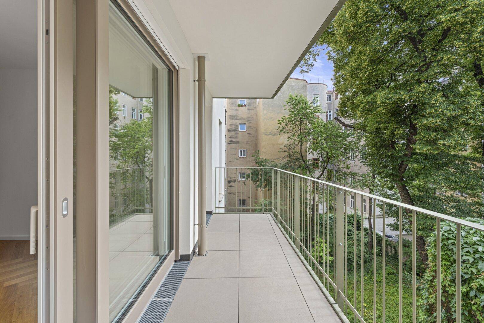 Heller Balkon mit Schiebetür zum Innenraum und grüner Aussicht auf den Innenhof.