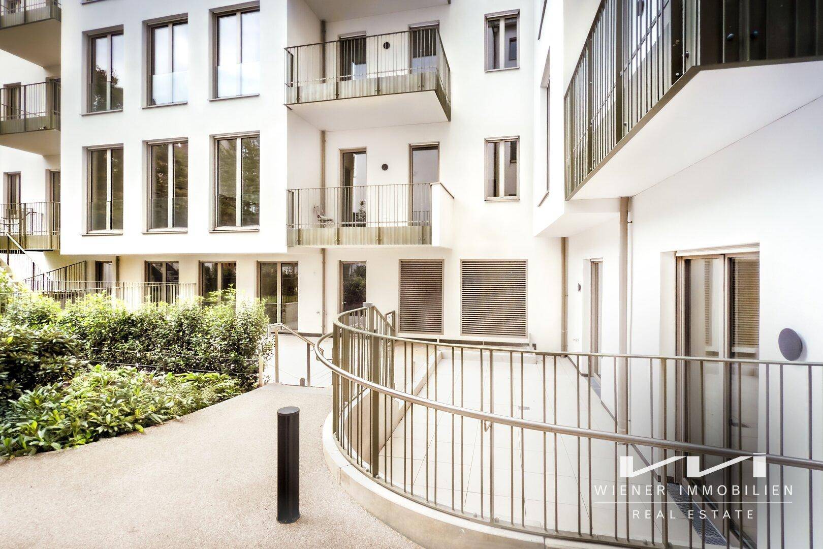 Barrierefreier Zugang über eine Rampe zu einem modernen Gebäude mit gepflegtem Innenhof.