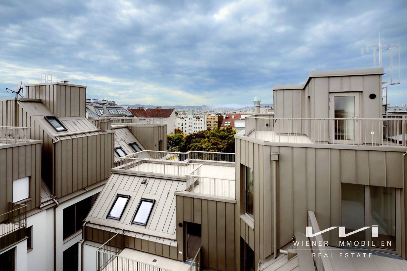 Weitläufige Dachlandschaft mit modernen Gebäuden, Terrassen und Blick auf die Stadt.