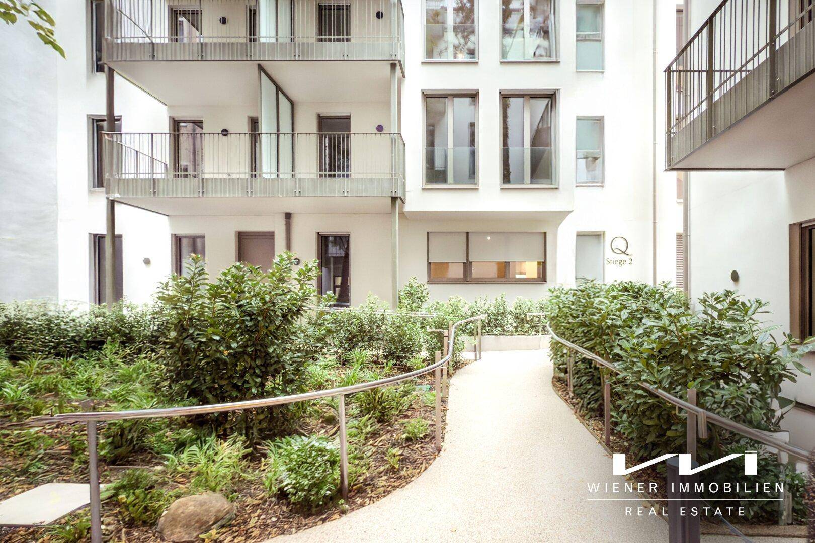Gepflegter Innenhof mit Grünflächen, Sträuchern und einem barrierefreien Weg zu den Gebäudeeingängen.