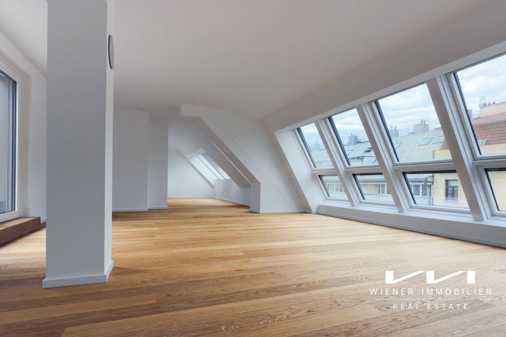 Heller Dachgeschossraum mit Holzboden, schrägen Decken und großen Fenstern für viel Tageslicht.