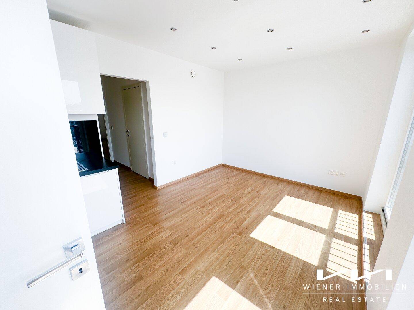 Geräumiger, heller Wohnraum mit Holzboden und weiß gestrichenen Wänden.