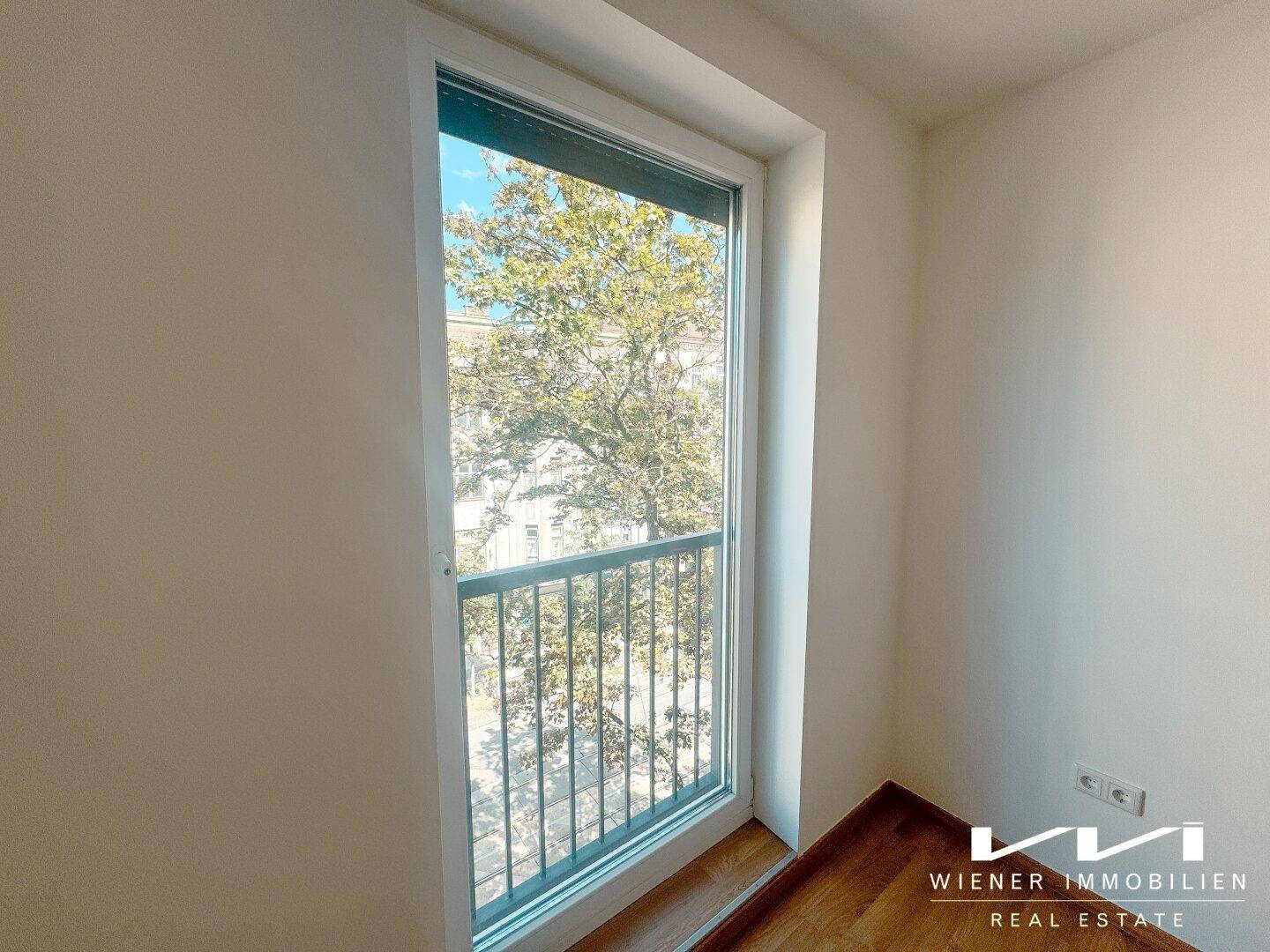 Helles Zimmer mit Holzboden und französischem Balkon, der einen Blick ins Grüne bietet.