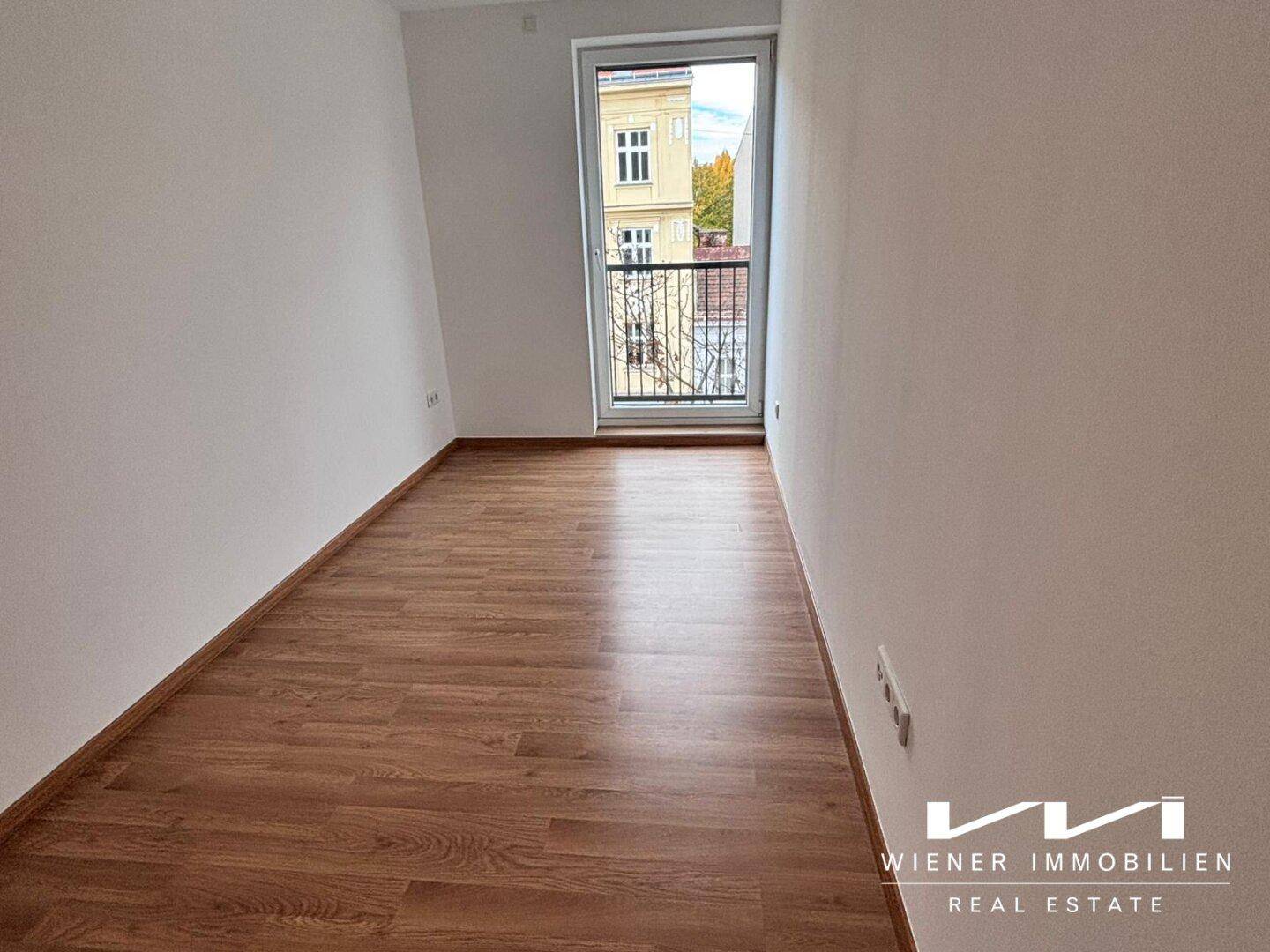 Leeres Schlafzimmer mit Holzboden und Zugang zu einem kleinen Balkon.