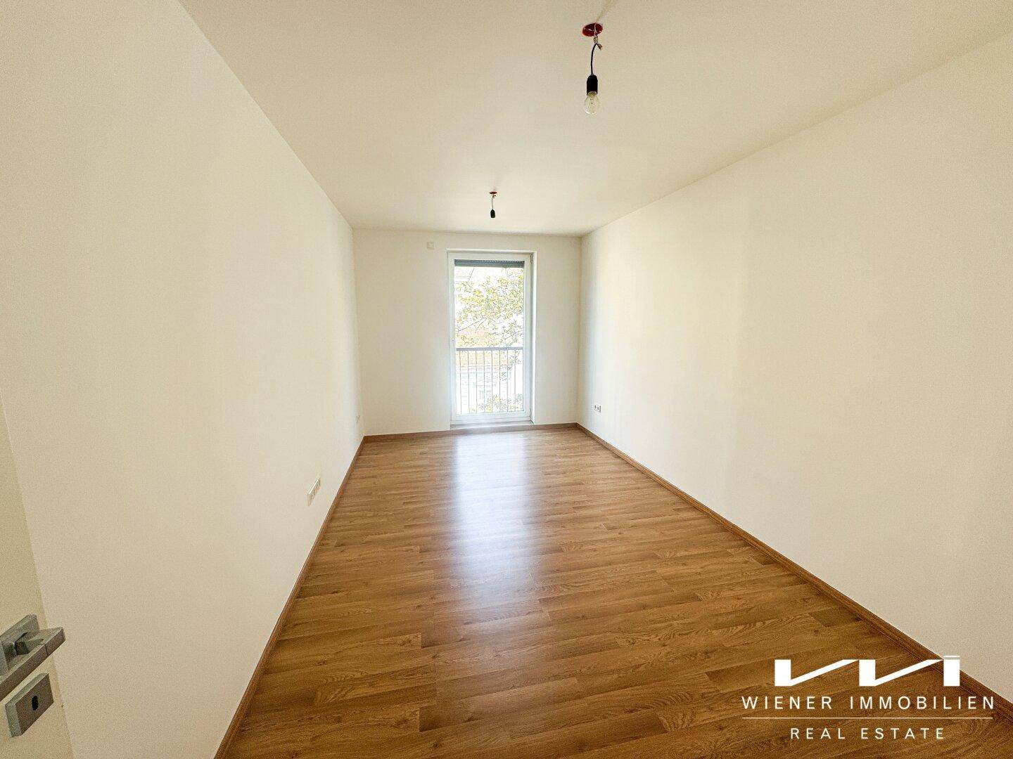 Geräumiges, leeres Schlafzimmer mit Holzboden und Balkonzugang.