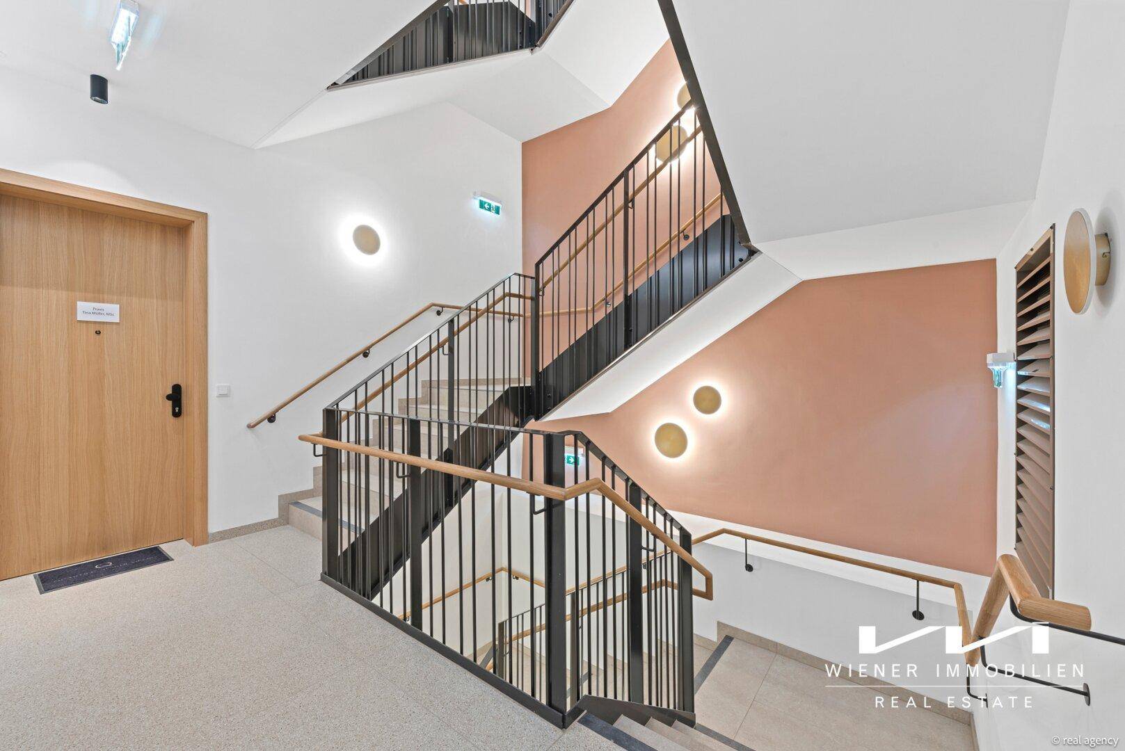 Modernes Treppenhaus mit Metallgeländer, Holzhandläufen und dekorativen Wandleuchten.
