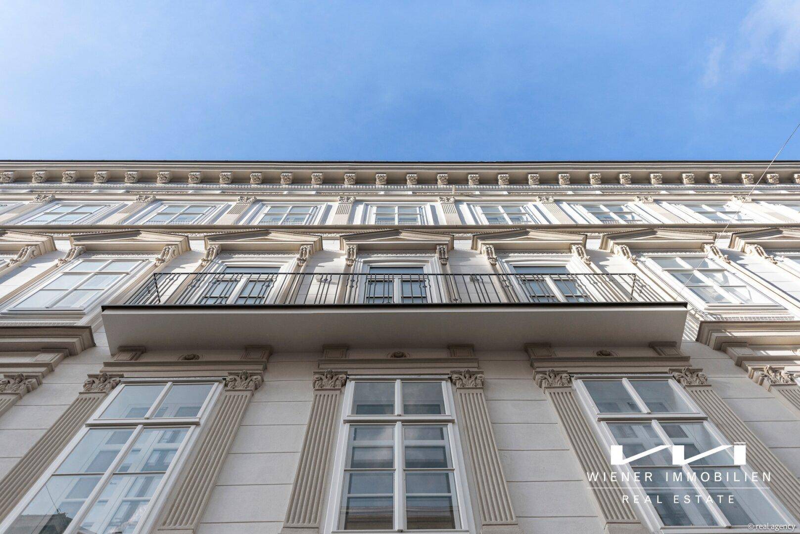 Historische Fassade eines Altbaus mit Stuckelementen und einem kleinen Balkon unter blauem Himmel.