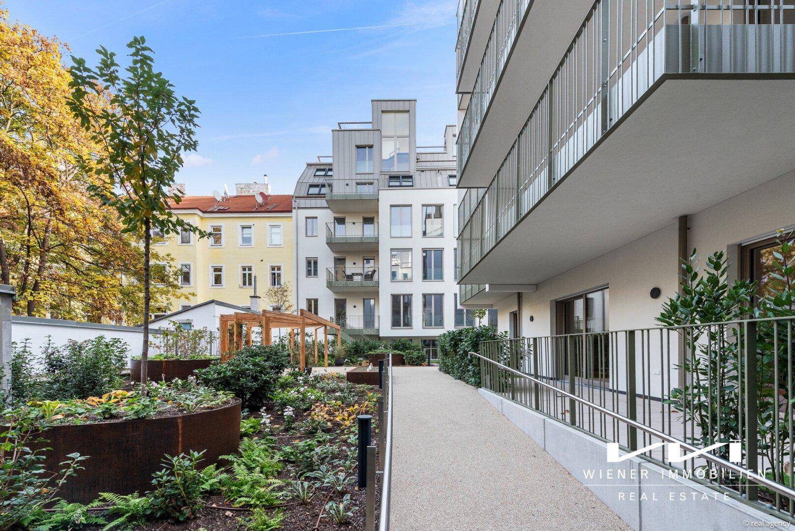 Gepflegter Gemeinschaftsgarten mit modernen Hochbeeten und barrierefreiem Zugang zum Gebäude.