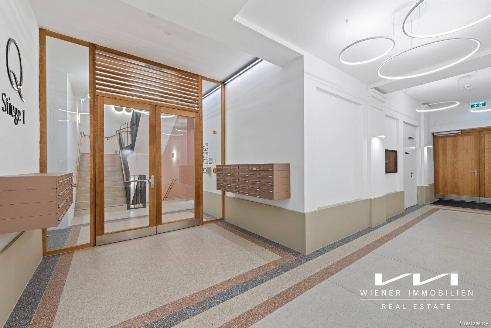 Heller Eingangsbereich eines Mehrfamilienhauses mit modernen Leuchten und Briefkästen.