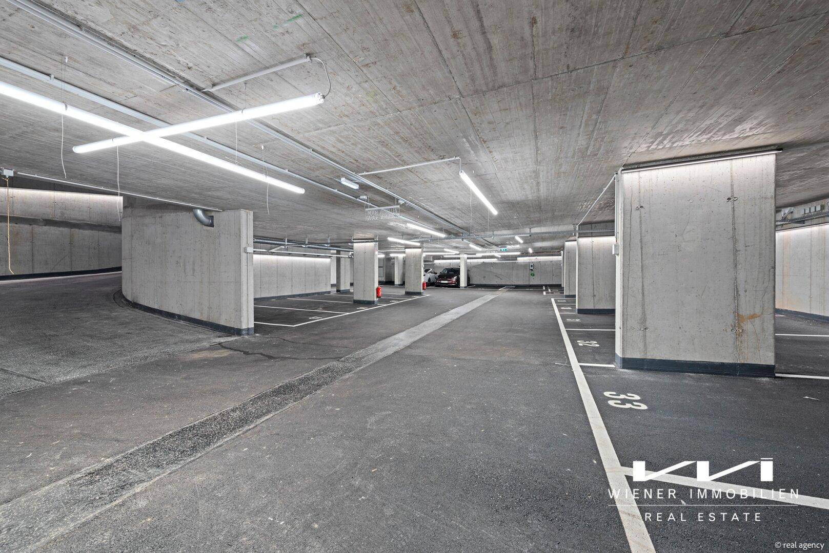 Geräumige Tiefgarage mit vielen Stellplätzen, Betonwänden und Deckenbeleuchtung.
