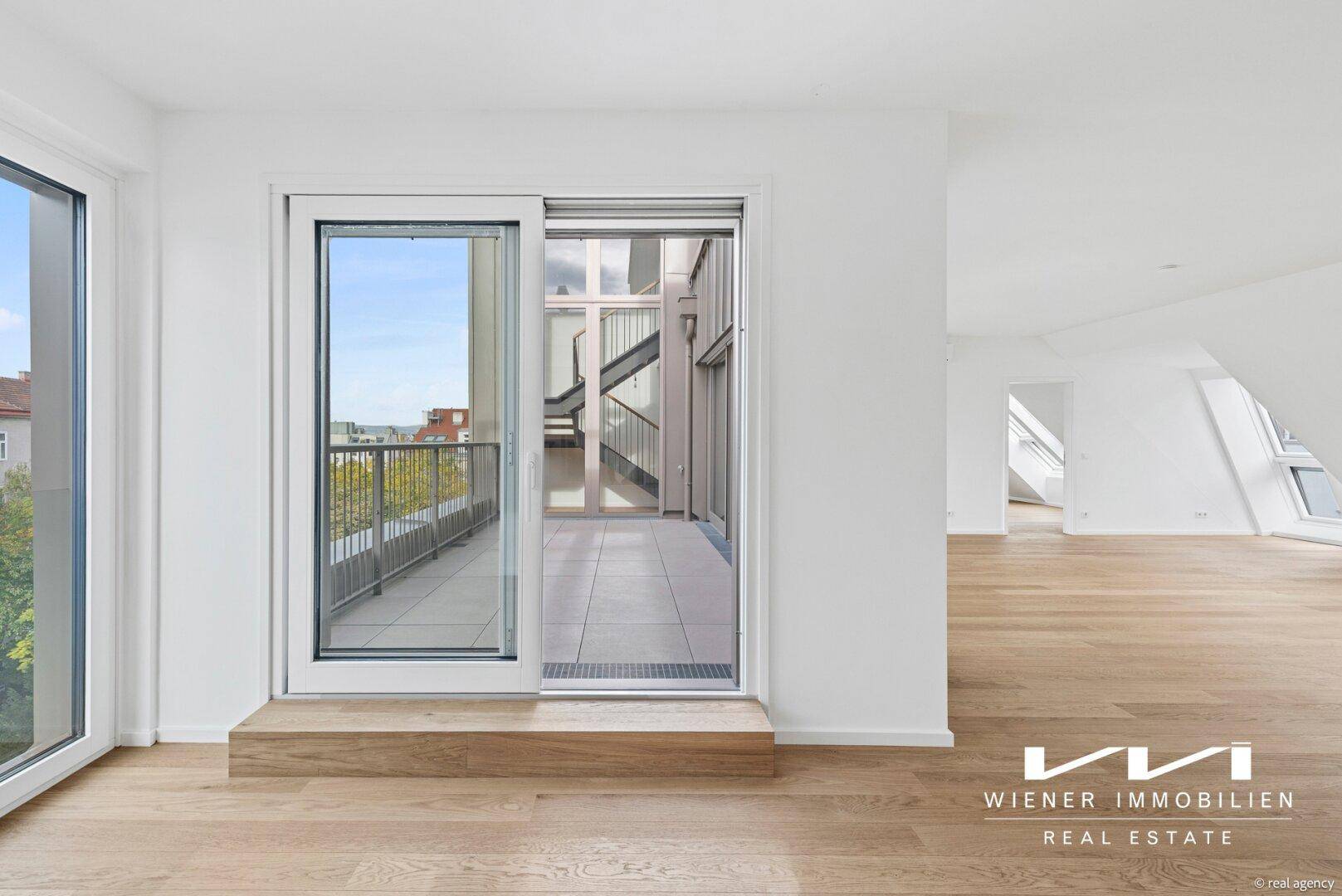 Heller Wohnraum mit Holzboden und Schiebetüren, die zu einem Balkon führen.
