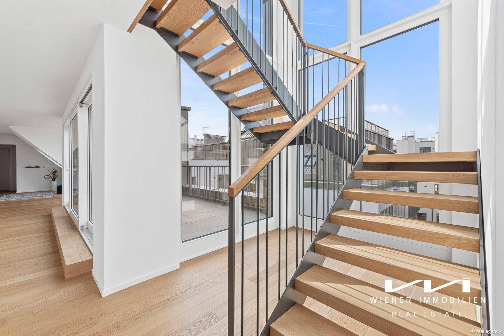 Moderne Holztreppe mit Metallgeländer, die zu den oberen Etagen führt, mit viel Tageslicht.
