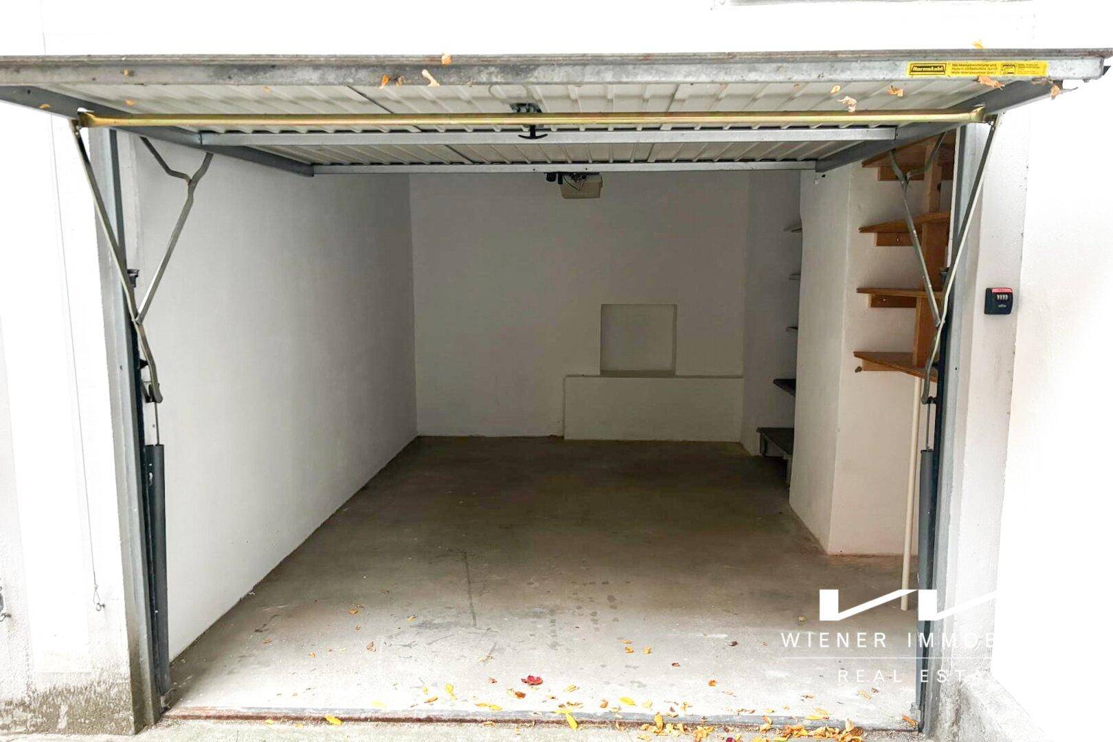 Geräumige Garage mit weißen Wänden, Betonboden und praktischen Holzregalen an der Seitenwand.