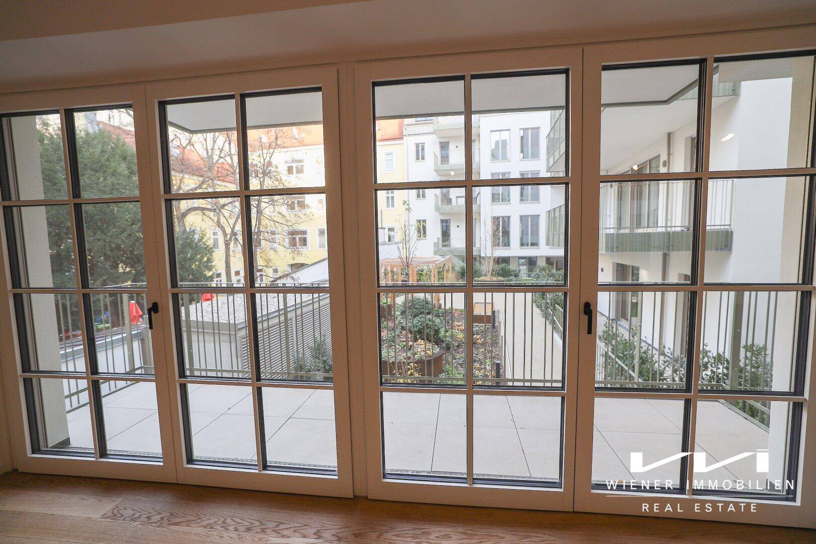 Große Sprossenfenster bieten einen schönen Blick auf den begrünten Innenhof der modernen Wohnanlage.