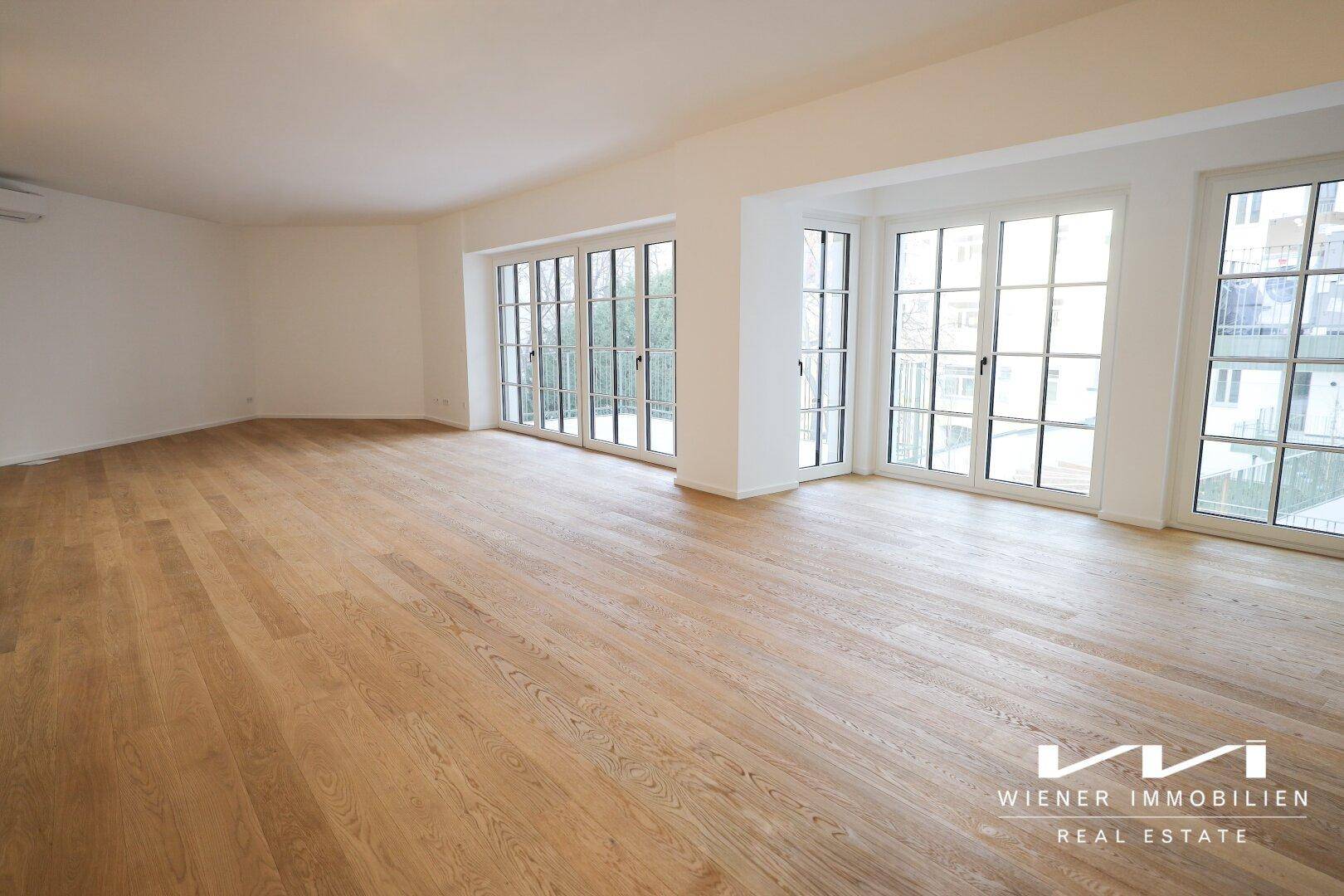 Lichtdurchfluteter Wohnbereich mit elegantem Holzparkett und großen Fenstern, die einen Blick nach draußen bieten.