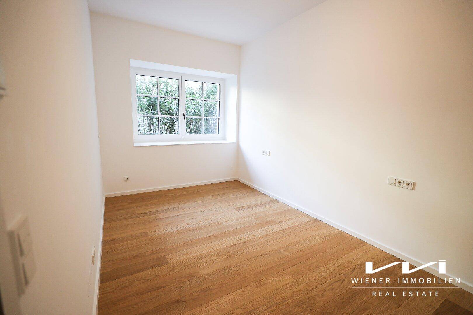 Ruhiges Schlafzimmer mit Holzparkett und einem Fenster, das viel Tageslicht hereinlässt.