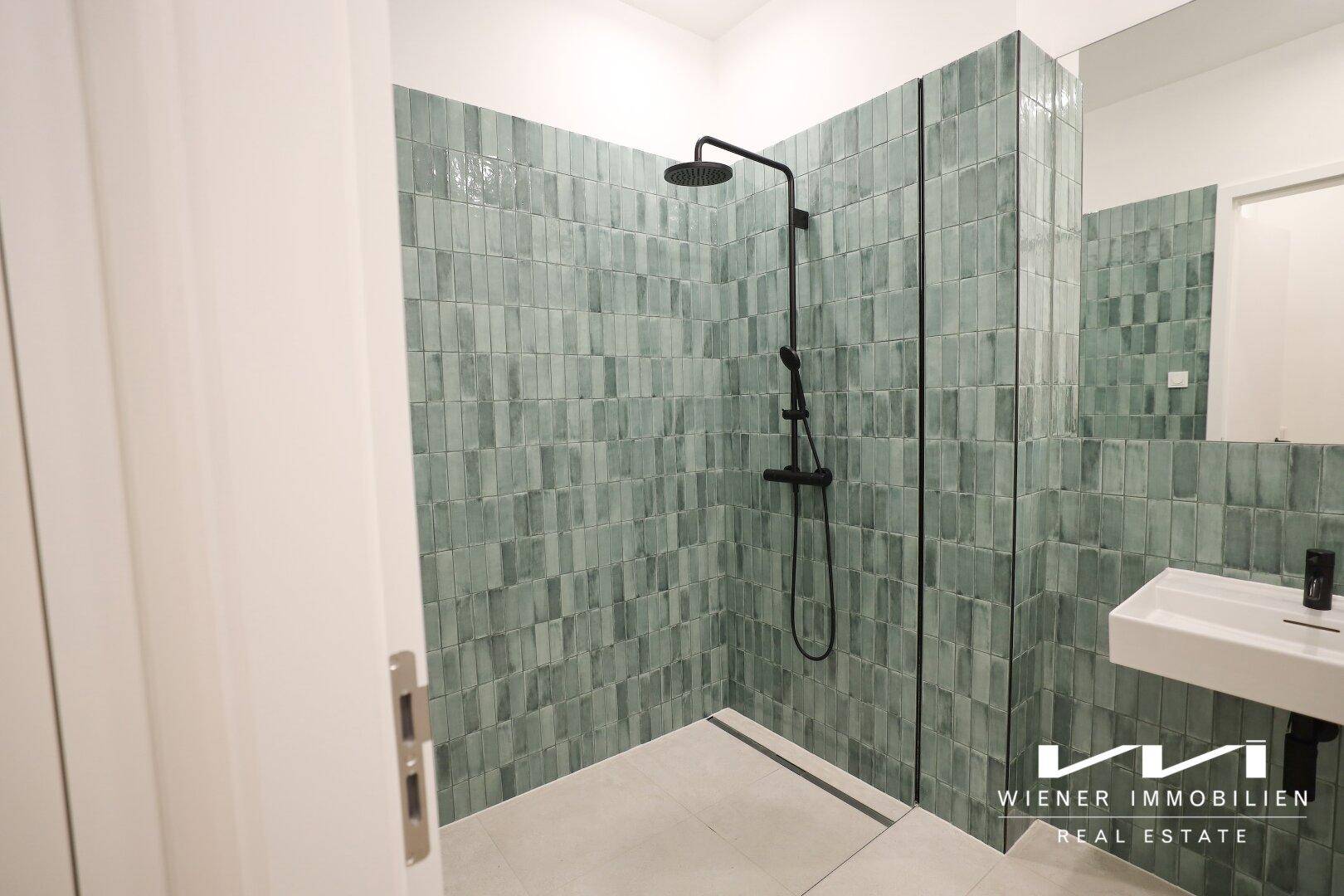 Modernes Badezimmer mit begehbarer Dusche, grünen Fliesen und minimalistischem Design.