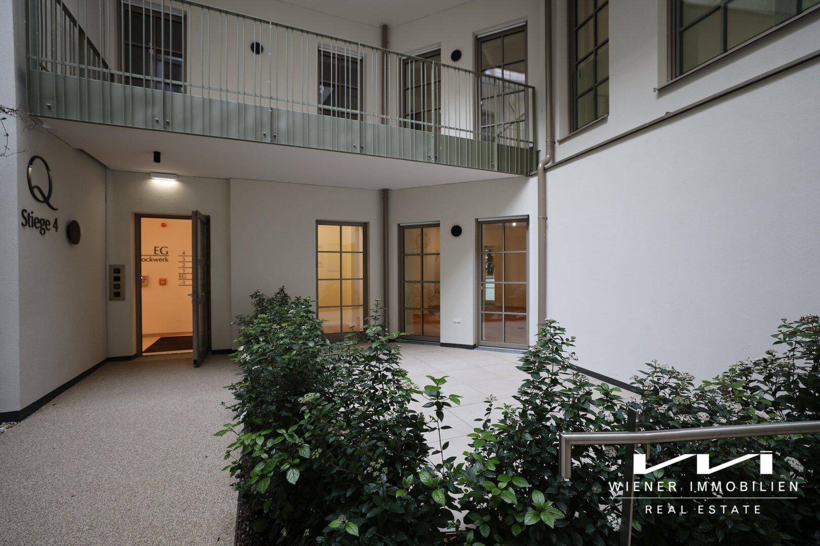 Ruhiger Innenhof mit Pflanzen und Zugang zu den Wohneinheiten des Gebäudes.