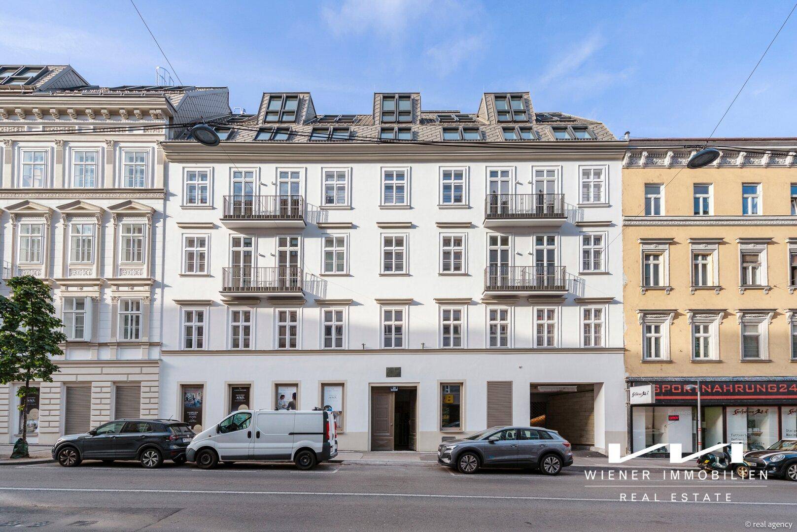 Frontansicht des historischen Gebäudes mit mehreren Balkonen und Dachfenstern, umgeben von anderen Stadtgebäuden.