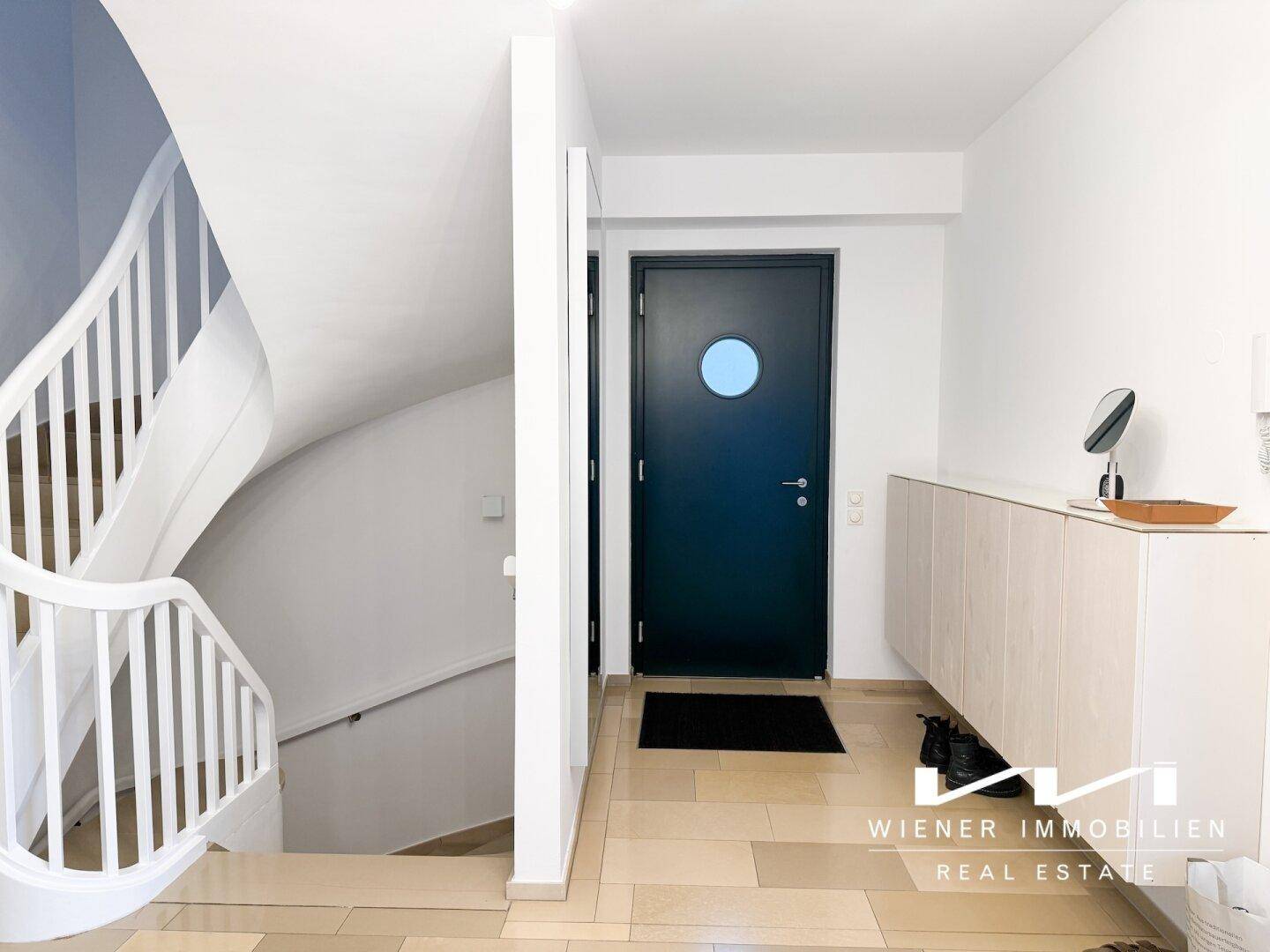 Heller Eingangsbereich mit moderner Tür, weißer Treppe und praktischem Sideboard.