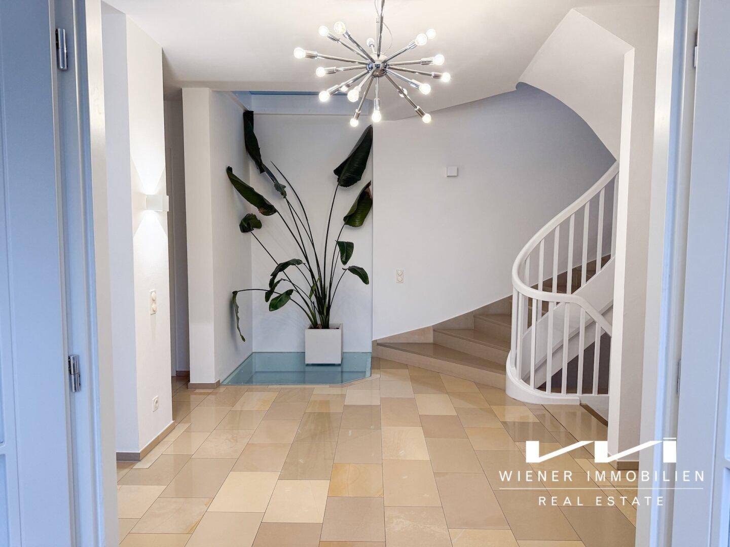 Geräumiger Eingangsbereich mit eleganter Wendeltreppe, großer Pflanze und modernem Kronleuchter.