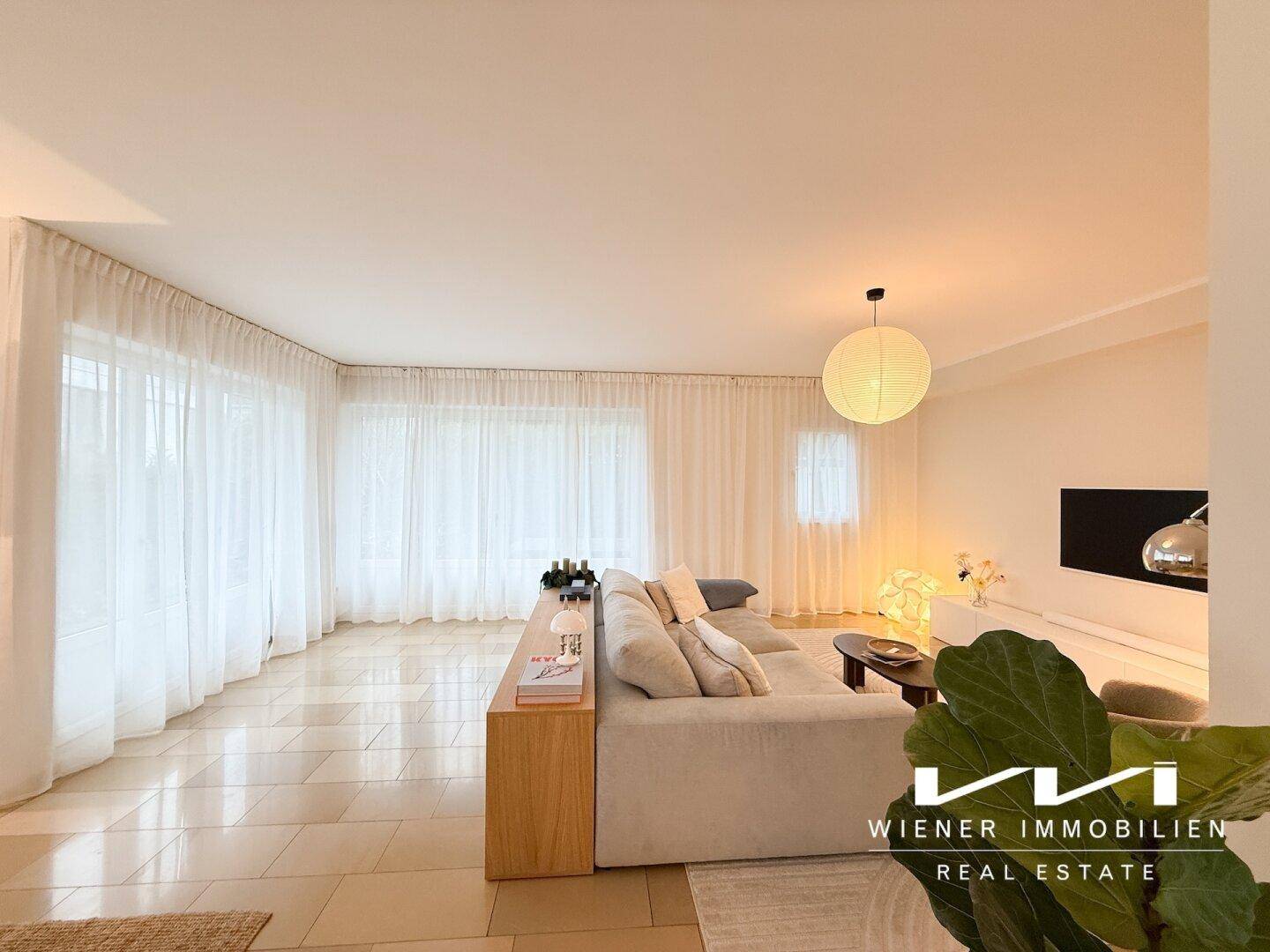 Gemütliches Wohnzimmer mit großem Sofa, stilvoller Beleuchtung und bodentiefen Fenstern.