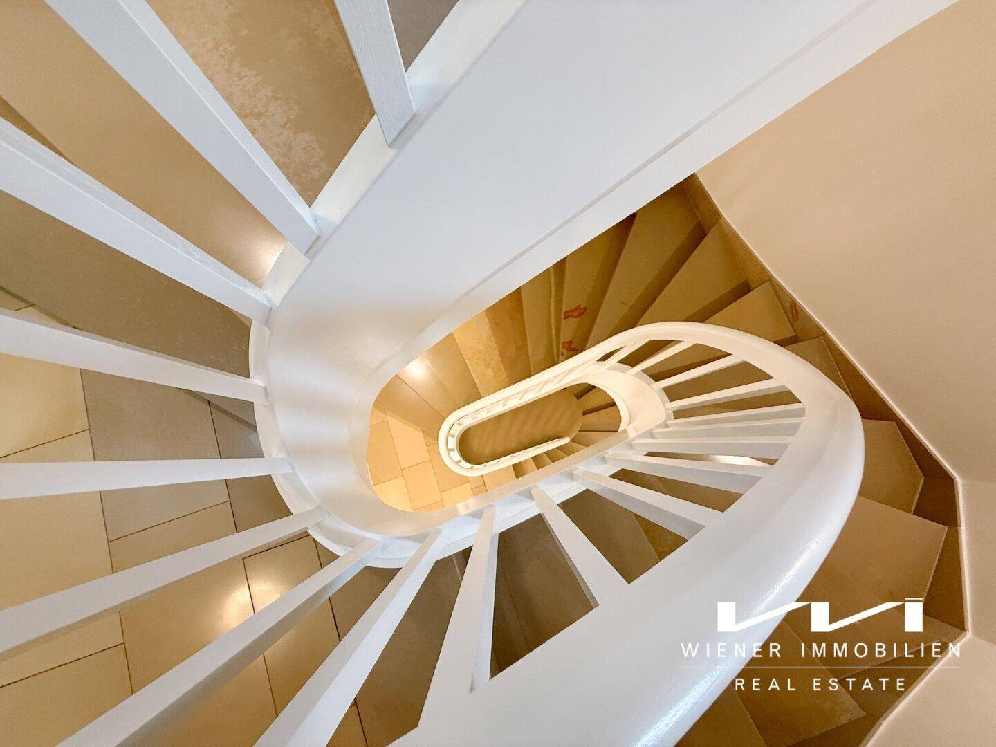 Elegante Wendeltreppe mit weißen Geländern und hellen Stufen, von oben fotografiert.