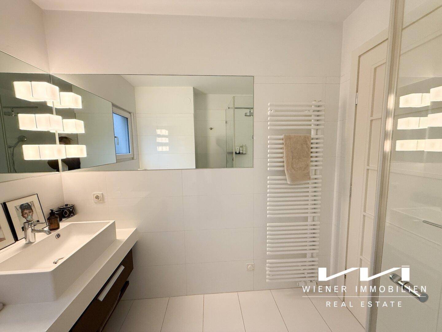 Modernes Badezimmer mit großem Spiegel, Einzelwaschbecken und beheiztem Handtuchhalter.
