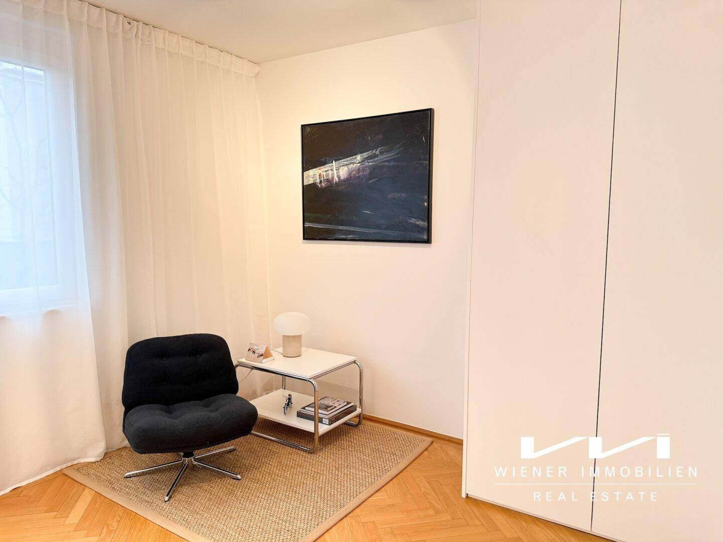 Helles Schlafzimmer mit modernem Sessel, kleinem Beistelltisch und weißem Kleiderschrank.