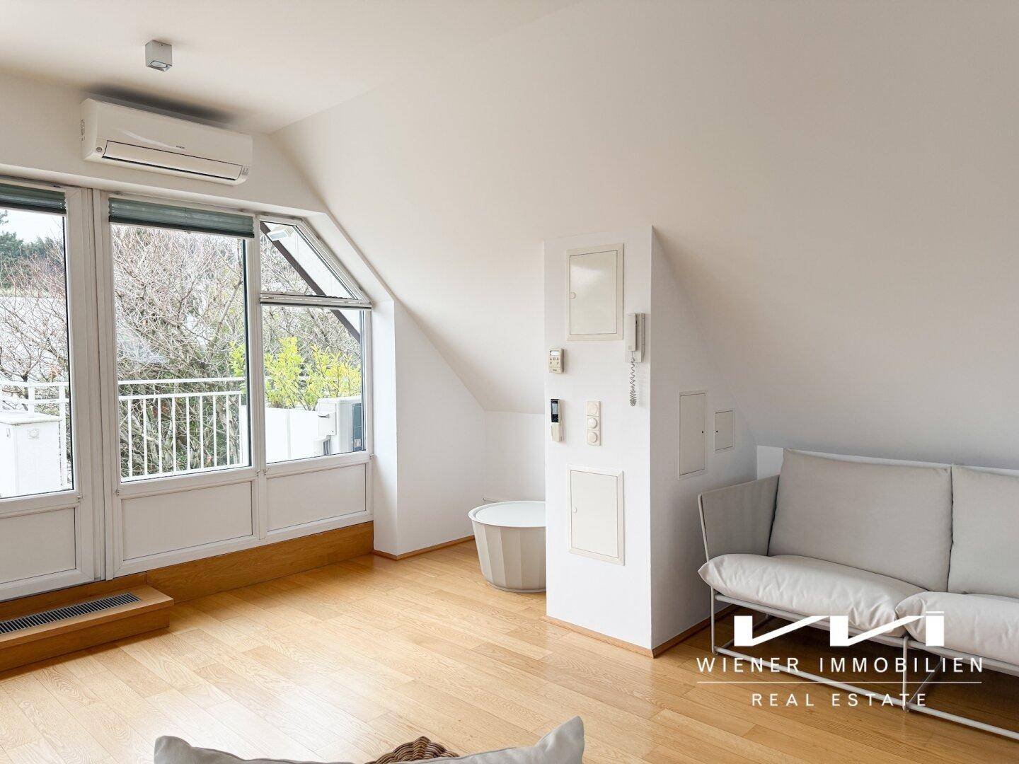 Helles Wohnzimmer im Dachgeschoss mit Schrägen, Klimaanlage und Zugang zu einer Terrasse.
