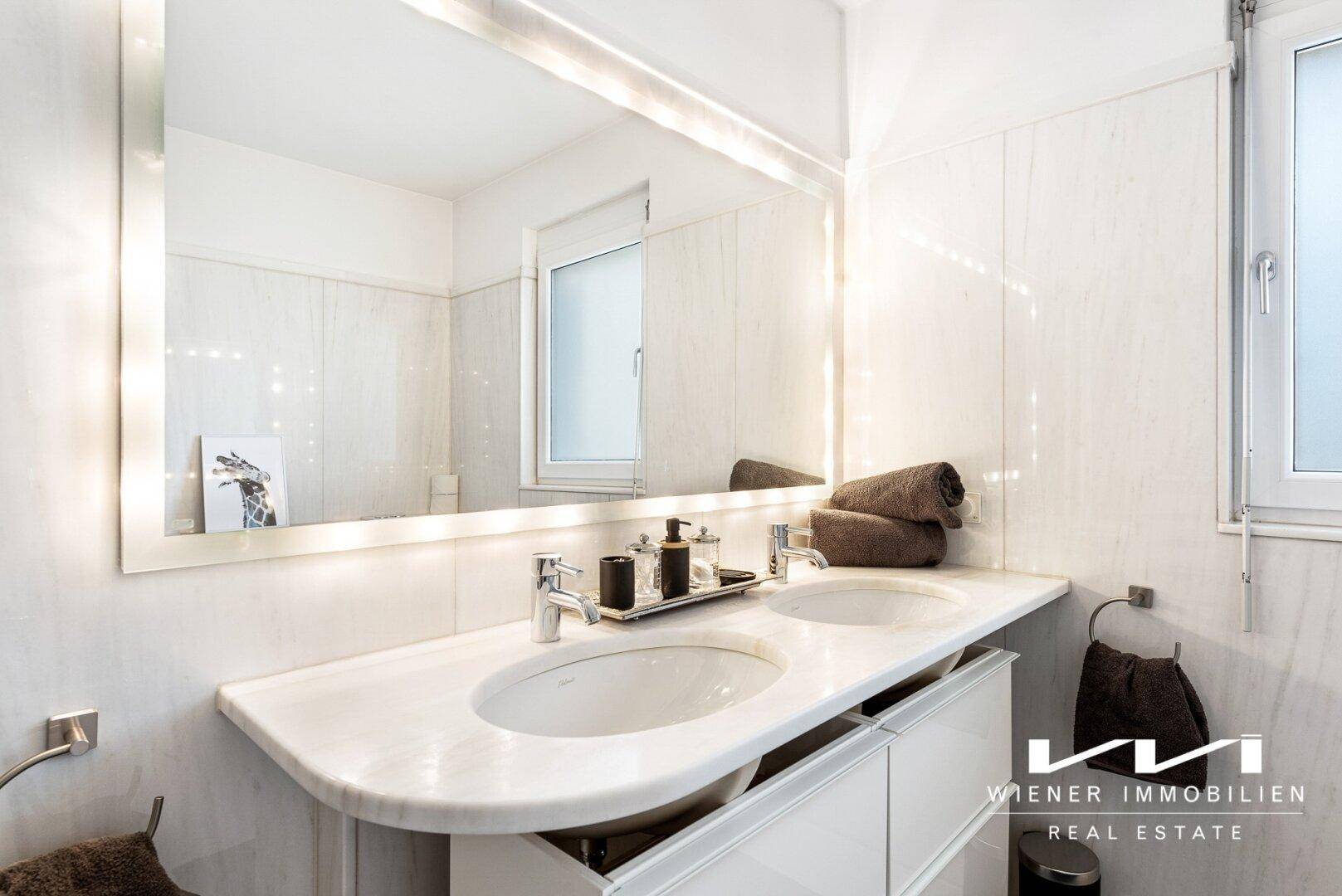Modernes Badezimmer mit Doppelwaschbecken, großem beleuchteten Spiegel und Fenster.