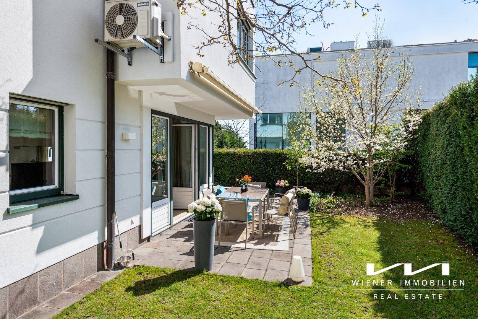 Sonniger Terrassenbereich mit Esstisch, umgeben von gepflegtem Rasen und einer hohen Hecke.