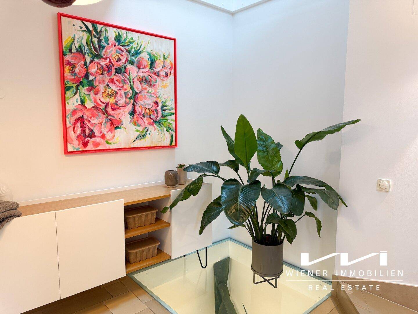 Heller Flurbereich mit dekorativer Pflanze, Kunstwerk und modernem Sideboard.