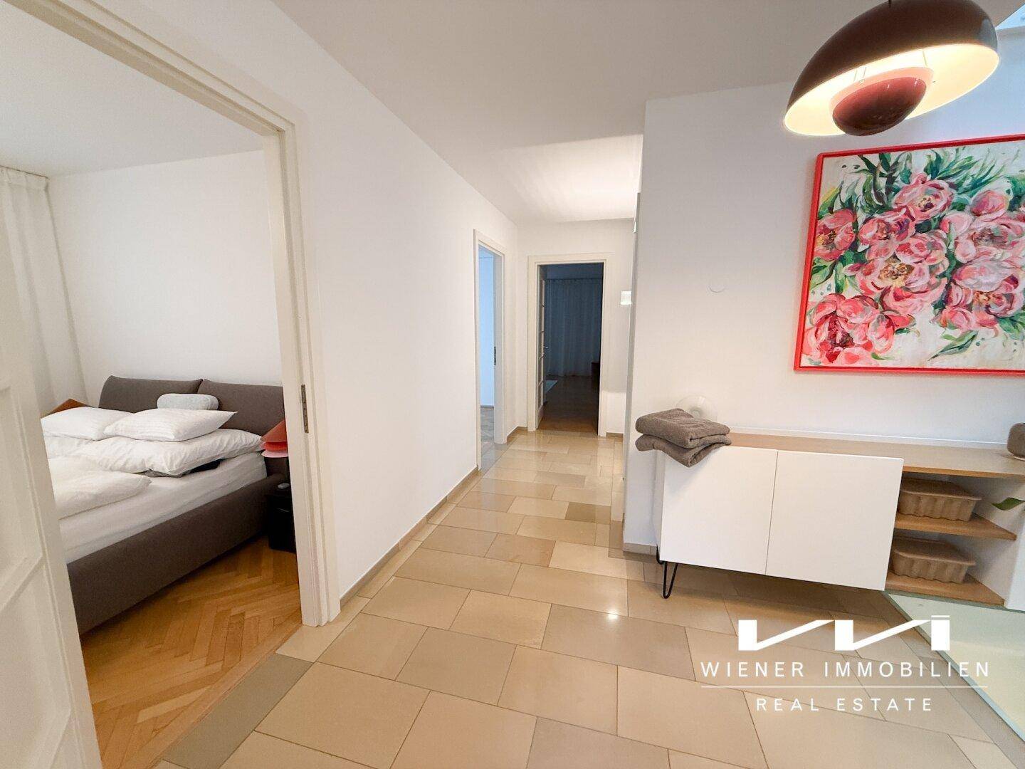 Heller Flur mit Fliesenboden, der zu einem Schlafzimmer mit Parkettboden führt.