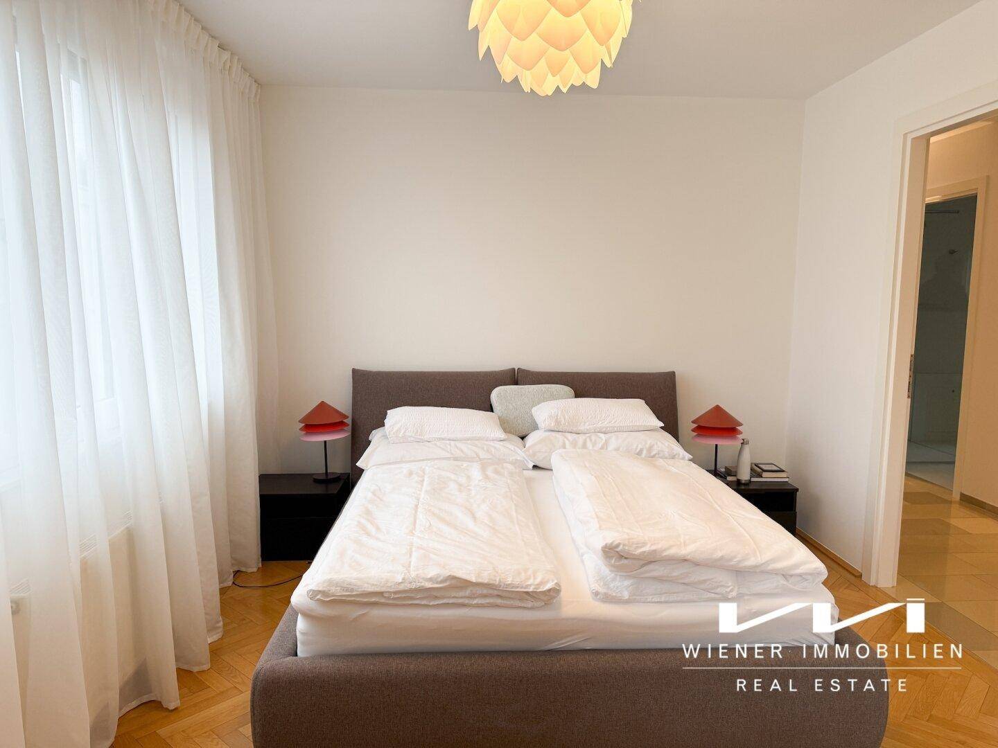Gemütliches Schlafzimmer mit großem Bett, hellen Vorhängen und Parkettboden.