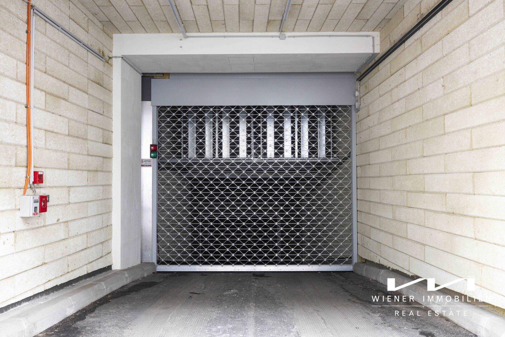 Eingang zu einer Tiefgarage mit einem robusten Metallrolltor und hellen Betonwänden.