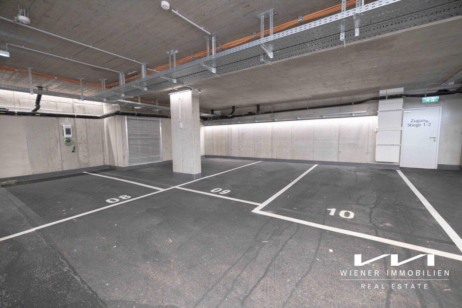 Geräumige Tiefgarage mit nummerierten Stellplätzen und sichtbaren Installationen an der Decke.