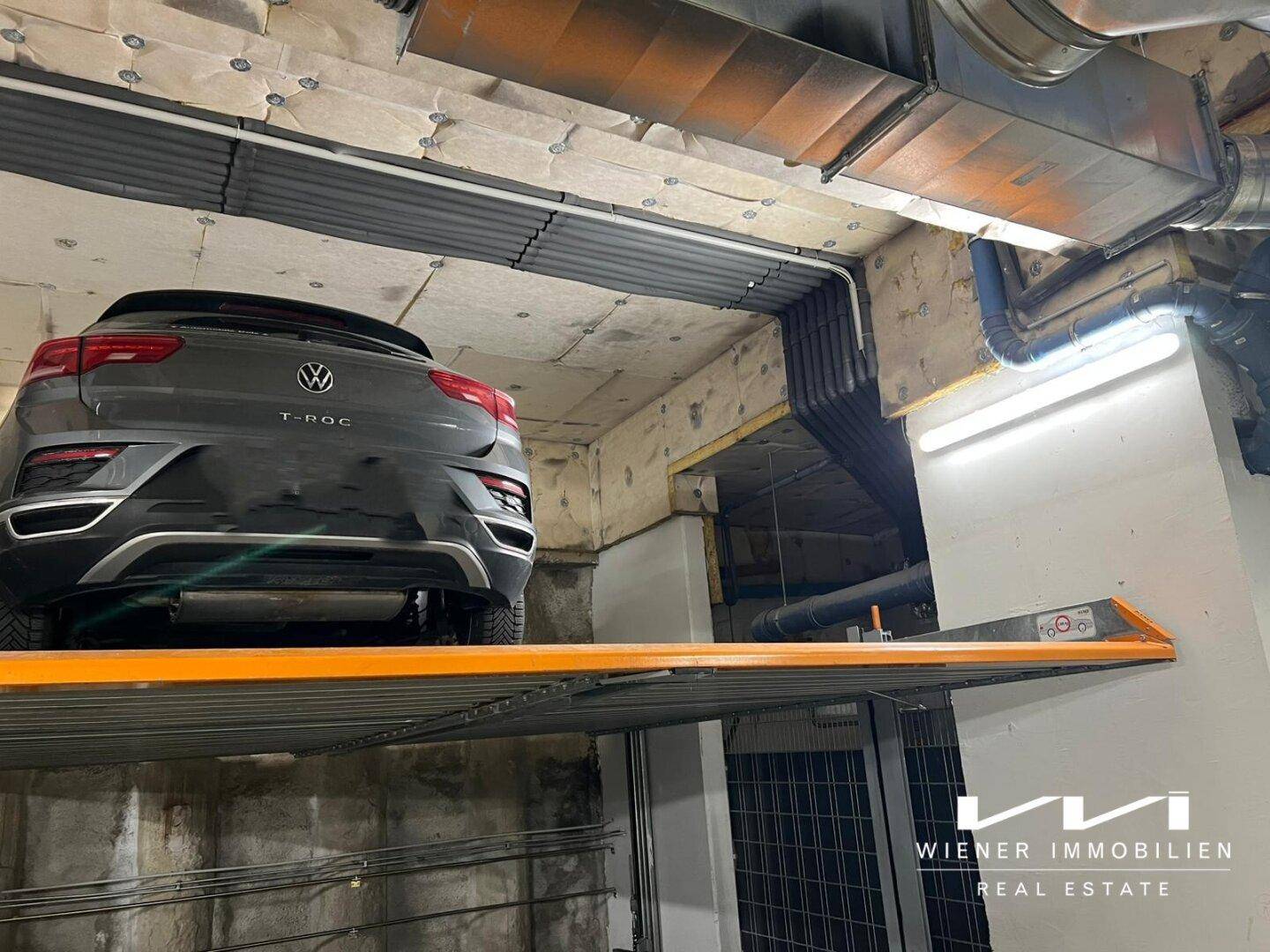 Nahaufnahme des mechanischen Parksystems mit Auto, sichtbaren Rohren und Betondecke in der Tiefgarage.