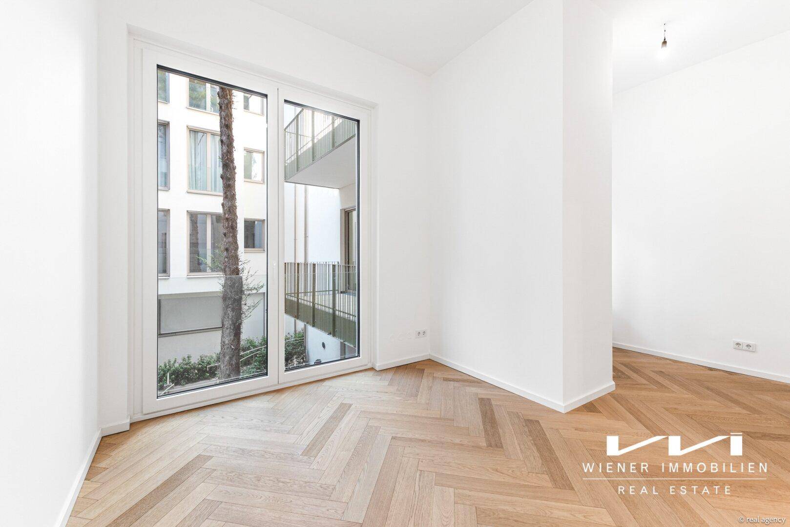 Lichtdurchflutetes Zimmer mit Fischgrätparkett und Zugang zu einem französischen Balkon.