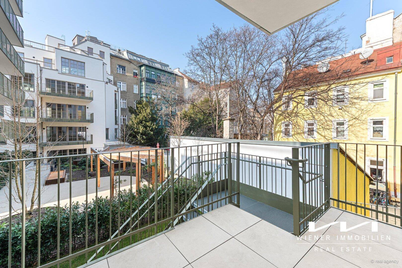 Balkon mit Blick auf den begrünten Innenhof und die umliegenden modernen Wohngebäude.